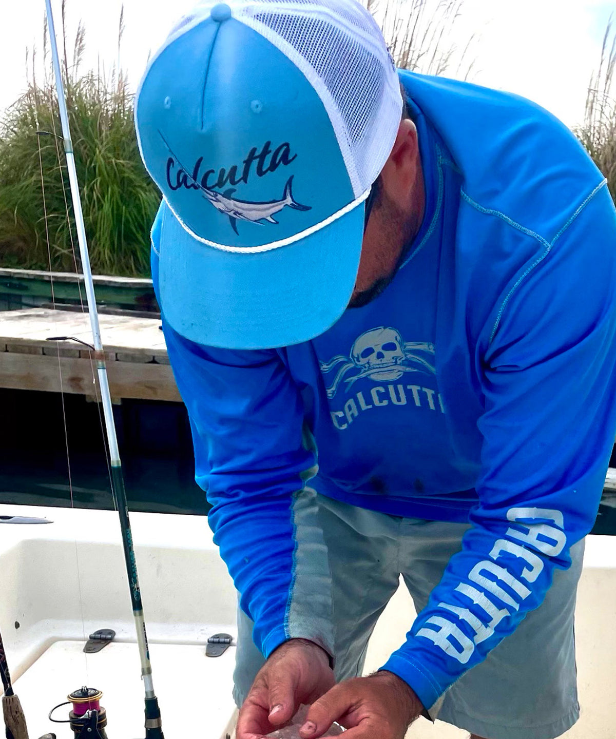 A man wearing a blue and white mesh trucker hat with Calcutta and a swordfish logo